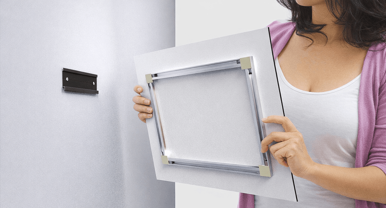 Person holding a print panel against a wall bracket, showing the FinoArt aluminium rail mount on the back