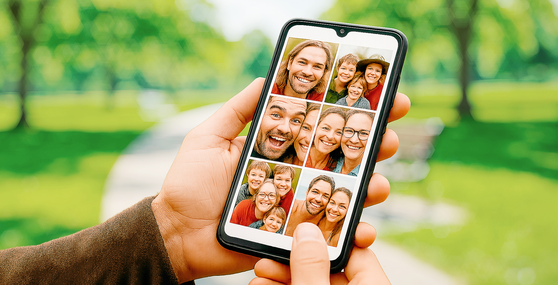 Hand holding smartphone with photo album open, in a park, showing grid of family photos