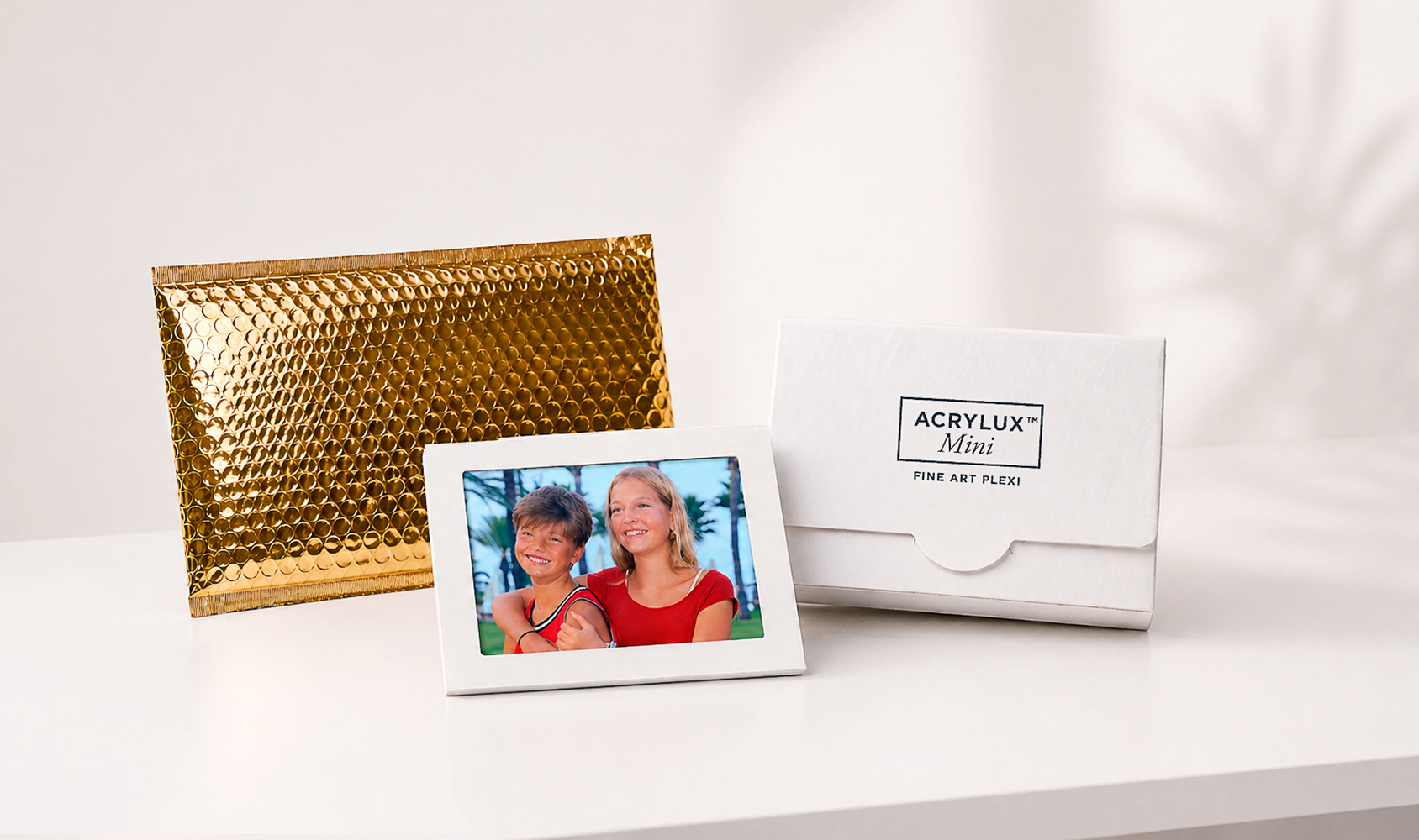 Panoramic view of Acrylux Mini gift packaging with gold envelope, framed photo print, and branded white presentation box