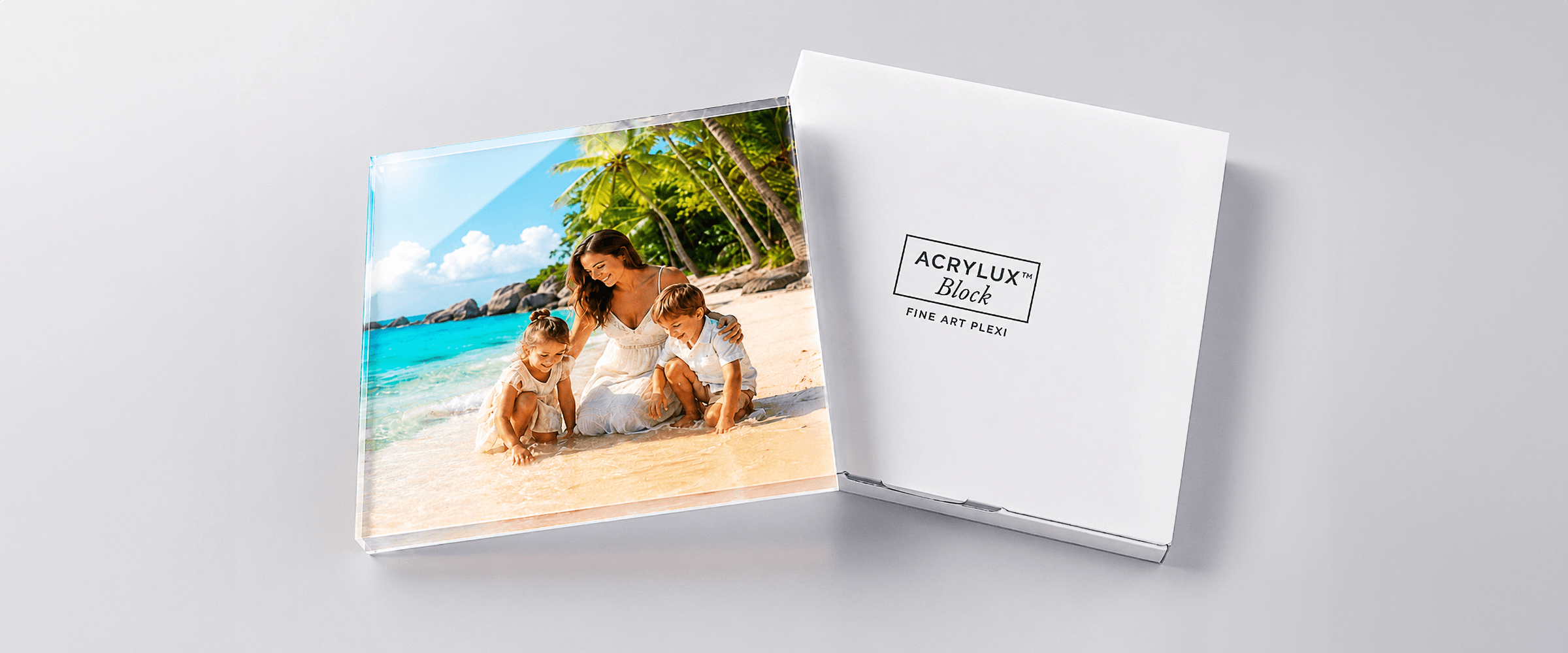 Acrylux Block acrylic photo print with tropical beach family scene next to elegant white gift box with Fine Art Plexi branding