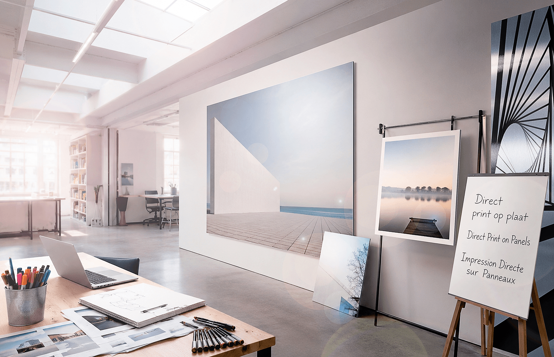 Modern photography studio displaying large format panel prints on walls and easels, with a workspace featuring a laptop and design materials