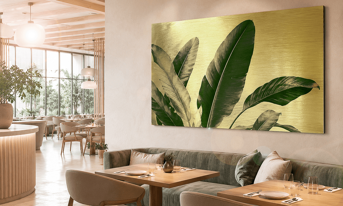 Tropical banana leaves on brushed gold dibond in a bright restaurant interior with velvet seating and natural light