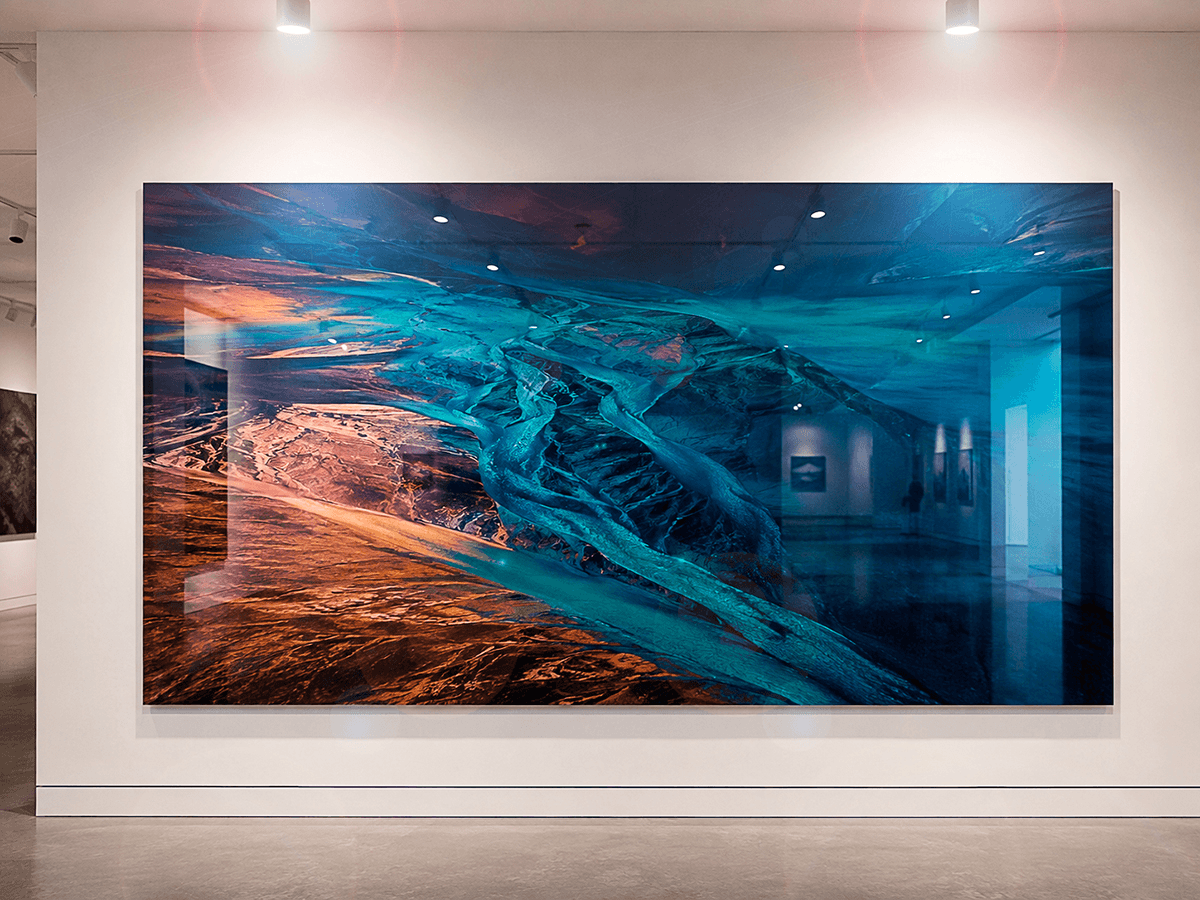 Large ChromaLuxe glossy print of an aerial glacial landscape in turquoise and rust tones, displayed as feature art in a professional gallery