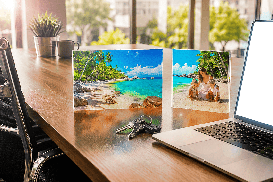Two Acrylux Block acrylic photo prints displaying tropical beach scenes on a wooden office desk with laptop and greenery
