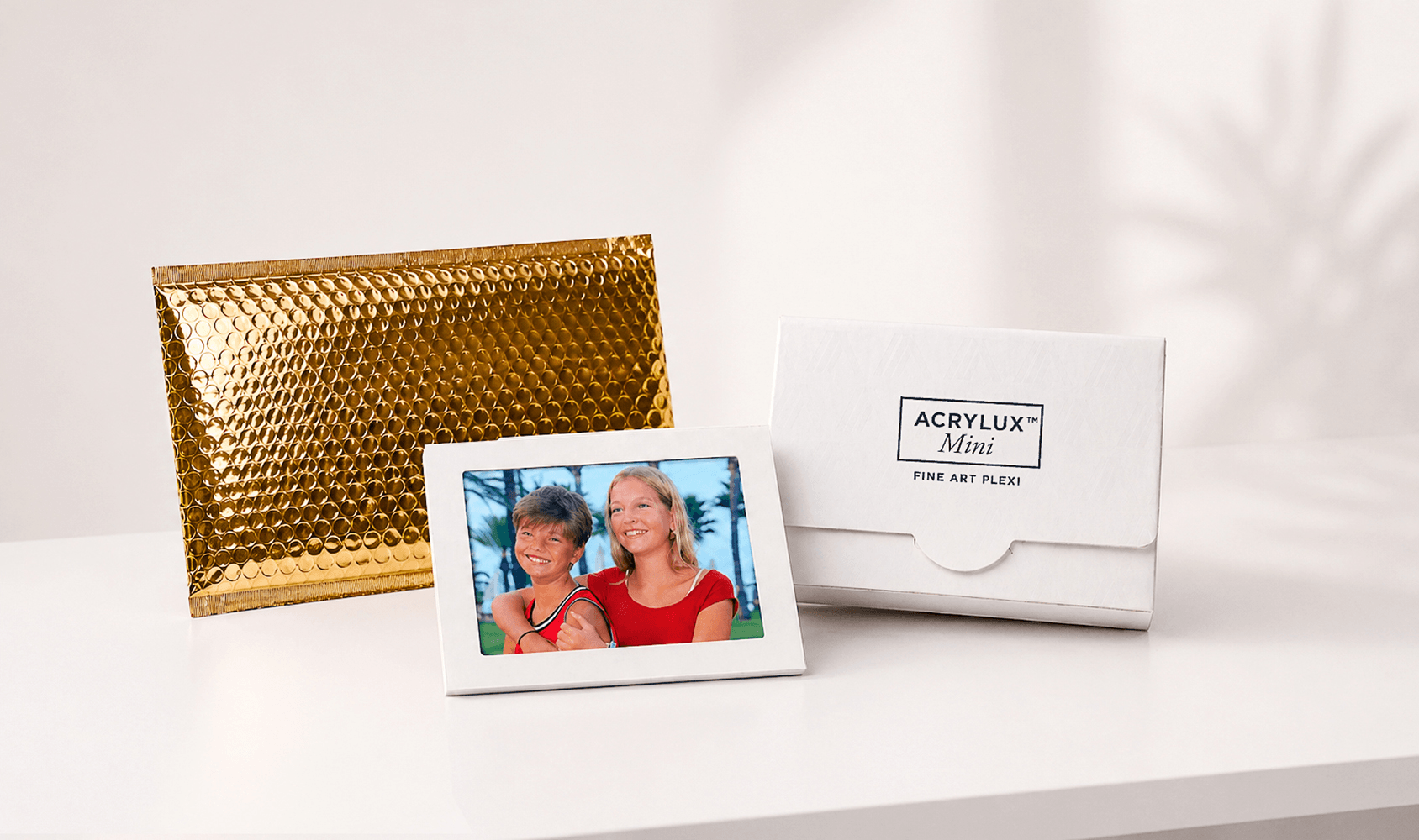 Panoramic view of Acrylux Mini gift packaging with gold envelope, framed photo print, and branded white presentation box
