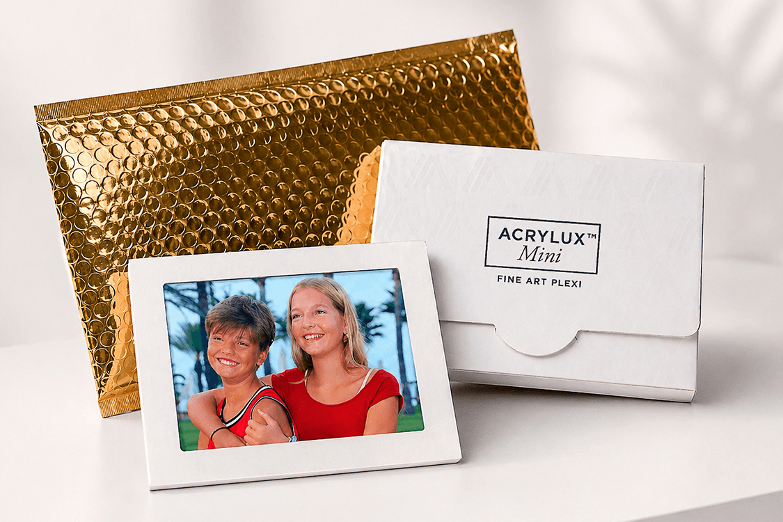 Acrylux Mini gift set with white branded box, acrylic photo frame showing two children, and gold metallic shipping envelope