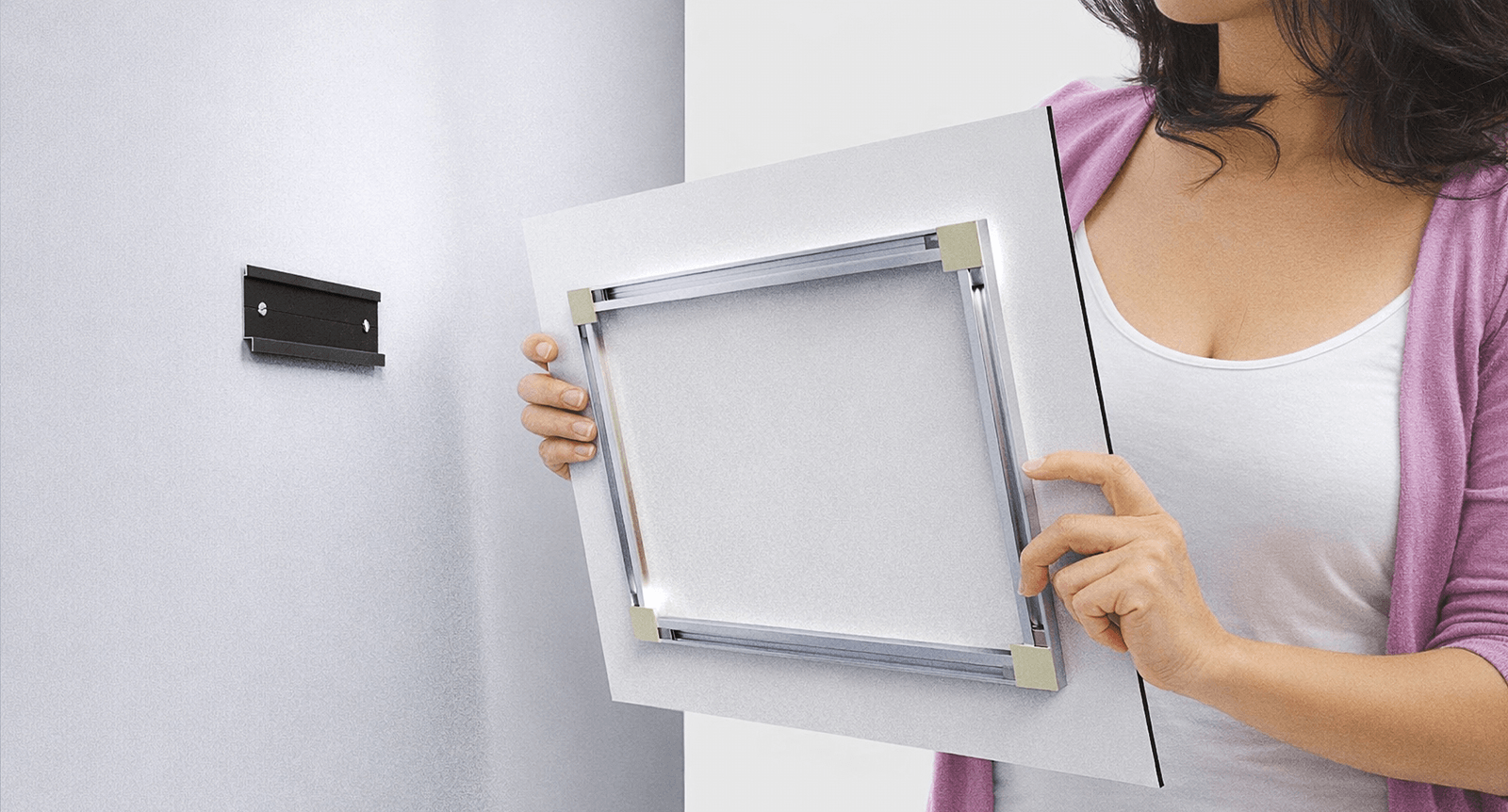 Person holding a print panel against a wall bracket, showing the FinoArt aluminium rail mount on the back