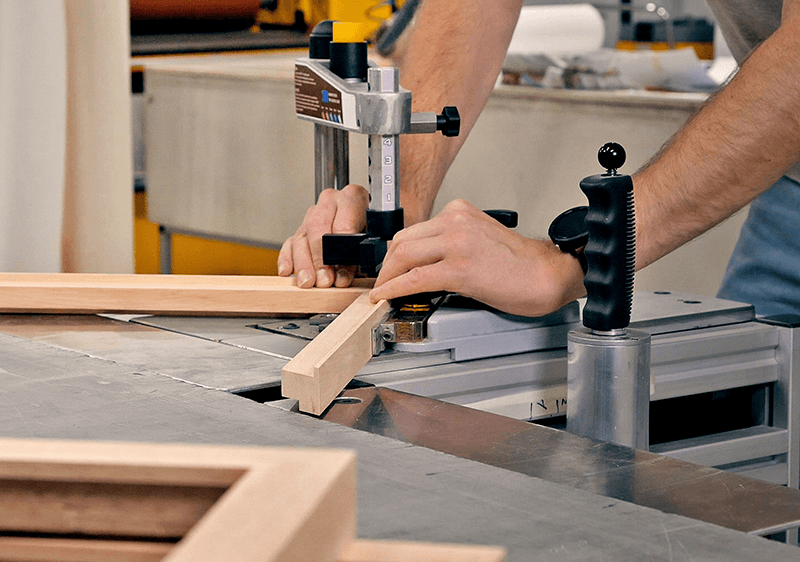 Craftsman assembling a custom wooden frame with a precision clamp in the framing workshop