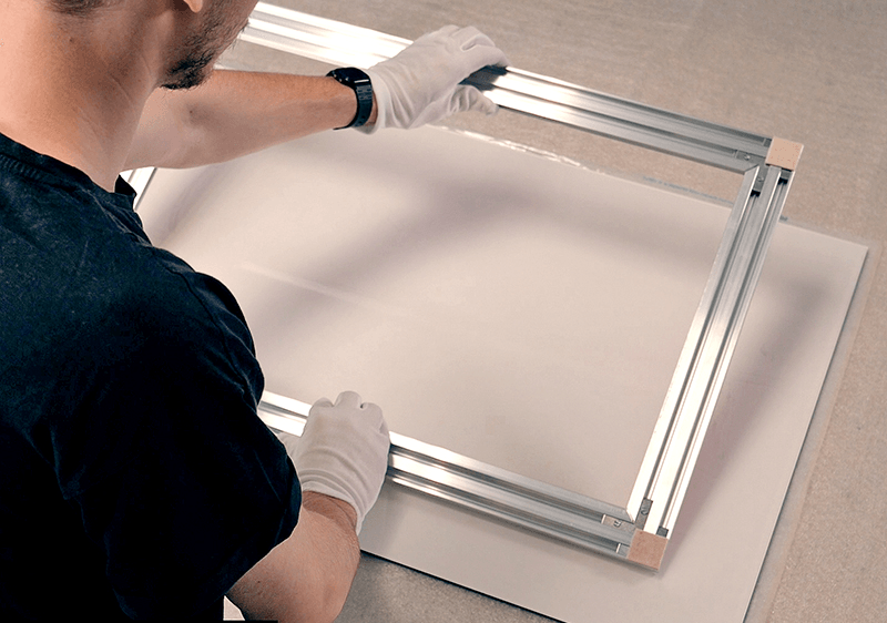 Technician with gloves attaching an aluminium hanging system to the back of a print