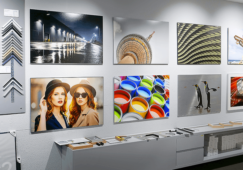 AuthenticPhoto showroom wall displaying various photo prints, frame samples, and finishing options